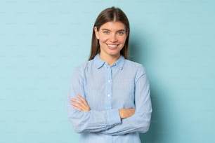 Head shot portrait of intelligent smiling woman standing with arms crossed against blue studio background. Successful confident entrepreneur and businesswoman looking at camera