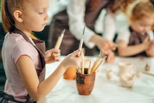 Girl stand near table and choose plastic knife to work with clay