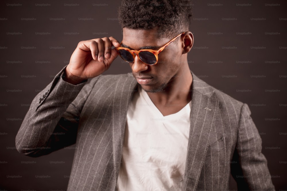 good looking African man in stylish sunglasses, suit jacket and white T-shirt on the black background. cool Afro guy