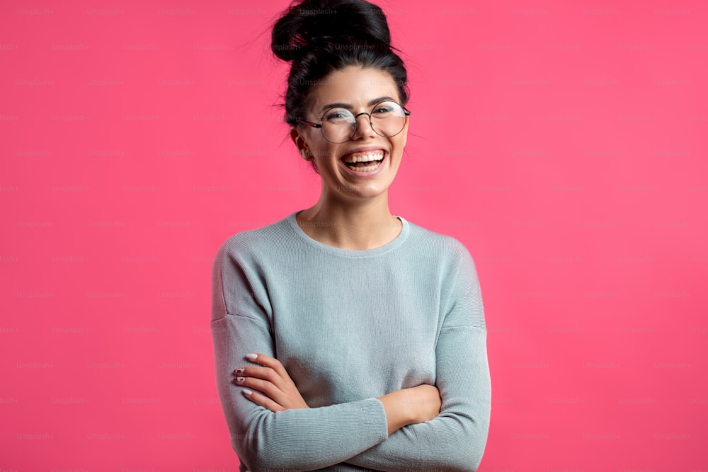 Hübsche lachende junge Frau mit Brille, isoliert auf dem rosa Hintergrund