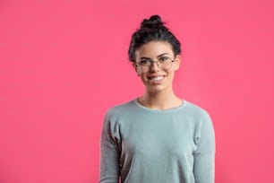 close up portrait of attractive happy girl in glasses wearing her black long hair up isolated on the pink background.