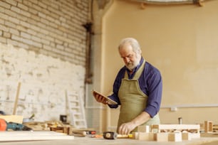 Retrato de vista lateral de cerca de un anciano con cabello gris, bigote y barba trabajando con tableta en el garaje. Espacio de copia