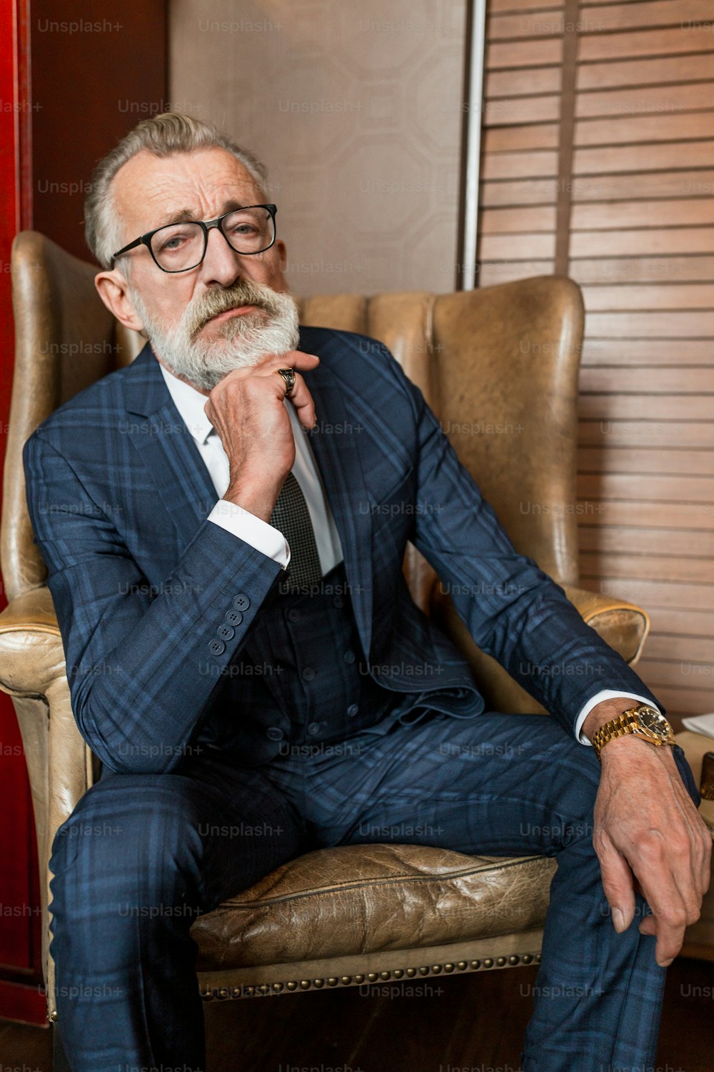Un anciano serio y concentrado lleva gafas y un traje azul formal, con rostro arrugado y experimentado, recordando momentos notables de la vida mientras está sentado en el restaurante.