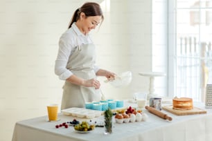 Alegre y hermosa chef femenina usando la cuchara para recoger la masa de magdalenas, foto de vista lateral de cerca. Espacio de copia