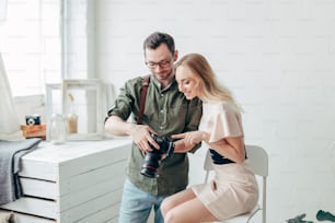menina sorridente incrível poiting na exibição da câmera enquanto conversava com um fotógrafo profissional dentro de casa