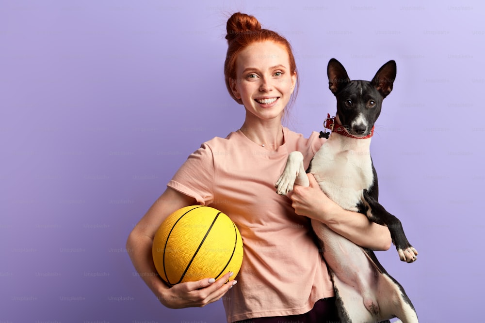 young ginger happy girl playing with her dog. isolated blue background, studio shot. entertainment, game, hobby, interest, lifestyle