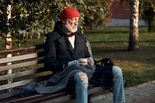 Mendigo mayor mirando desesperadamente la calle vacía, esperando dinero, ayuda. Vestido con sombrero rojo y abrigo cálido