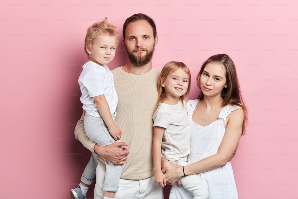 Glückliche junge Familie mit entzückenden kleinen Töchtern, die auf rosa Hintergrund posieren, Nahaufnahme, solierte rosa Hintergrund-Studioaufnahme. Beziehung