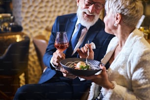 Hombre caucásico con traje y anteojos, hermosa mujer en blanco elegante blazer disfrutar de la comida en un lugar atractivo. Postre dulce y copa de champán. Amor en el aire