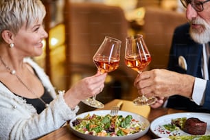 Beautiful elderly couple have a meal in personable restaurant, in love. Grey-haired male and female drink and clink glasses with champagne.
