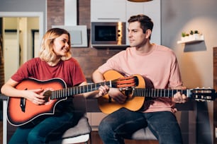 Dos jóvenes caucásicos, hombre y mujer sentados escuchando y tocando la guitarra, autodidactas