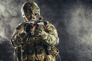 Uomo soldato delle forze speciali che tiene la mitragliatrice e l'equipaggiamento militare nello spazio fumoso