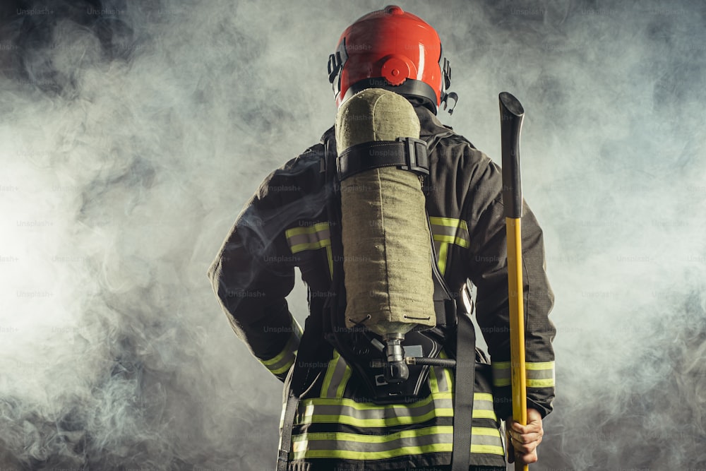 消防署で働く敬虔で自信に満ちた男の背面図は、緊急事態で人々を火事から救う準備ができており、制服とヘルメットを着用しています。