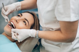 retrato da mulher loira jovem de boa aparência no exame odontológico, tratando os dentes na clínica ortodôntica profissional