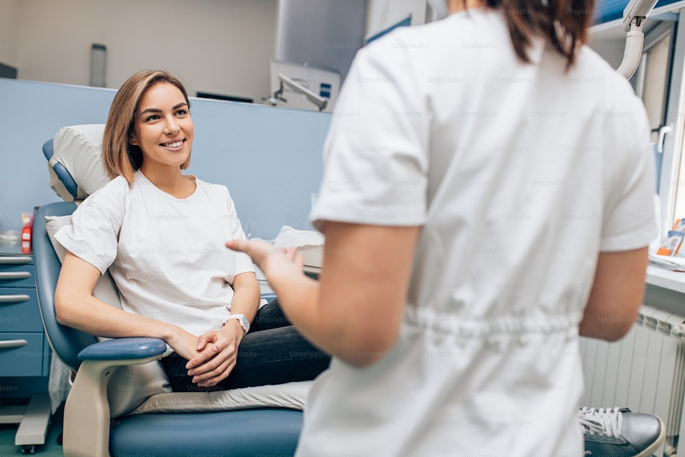 friendly doctor dentist examine teeth of caucasian young woman in casual wear, isolated in dentist office, using special medical equipment