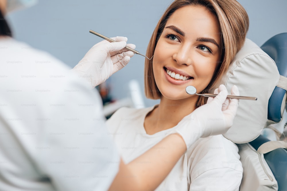 Une belle femme aux cheveux courts s’assoit dans un cabinet dentaire et regarde le médecin avec confiance, elle a un sourire parfait. Médecin professionnel de la clinique utiliser des instruments médicaux stérilisés spéciaux