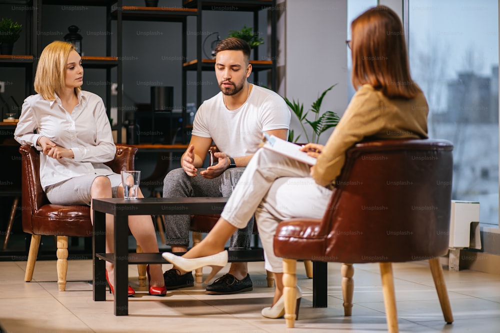 caucasian couple explaining to professinal psychologist situation inside of family and listening advices and ways of solving problems. lady psychologist nicely lead the conversation with patients in her own modern office