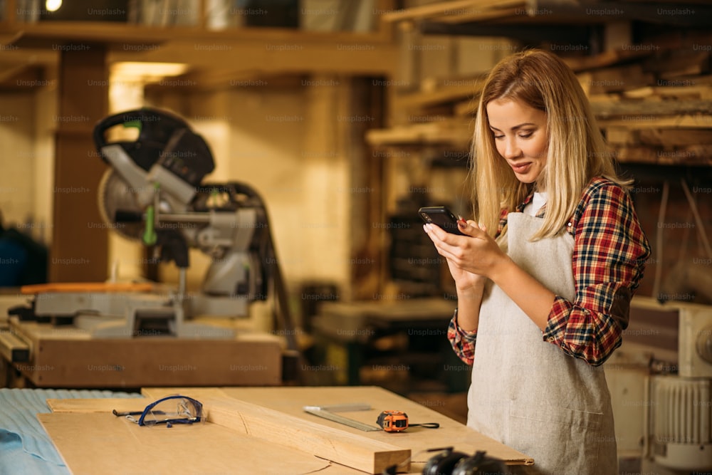 beautiful carpenter lady with smartphone, woman chat with friend while she has free time at work