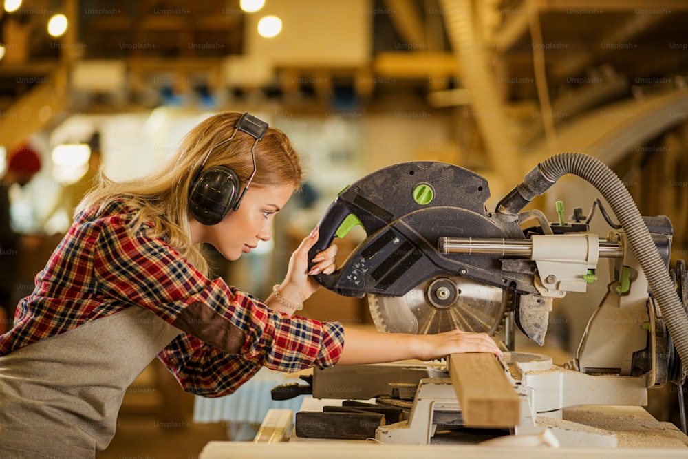 caucasian woman carpenter drives a circular saw, concentrated woman work in factory contrary to opinion that this is a man s job. feminism concept