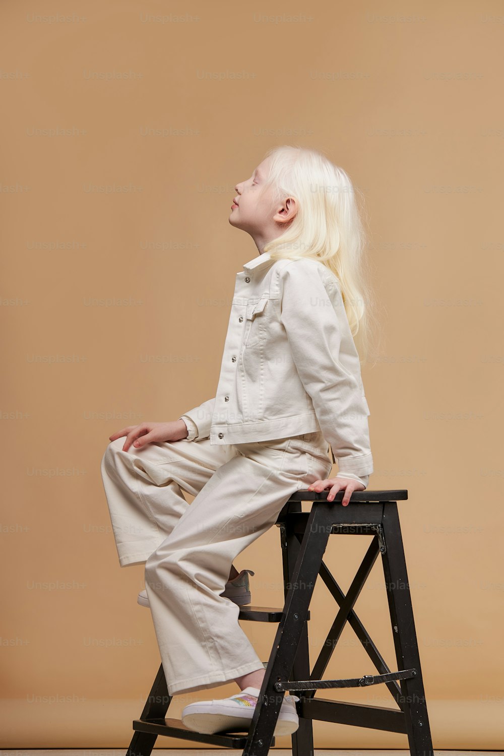 little caucasian girl is gentle fashion model, girl with unusual pale skin and white hair posing, sit on chair. side view