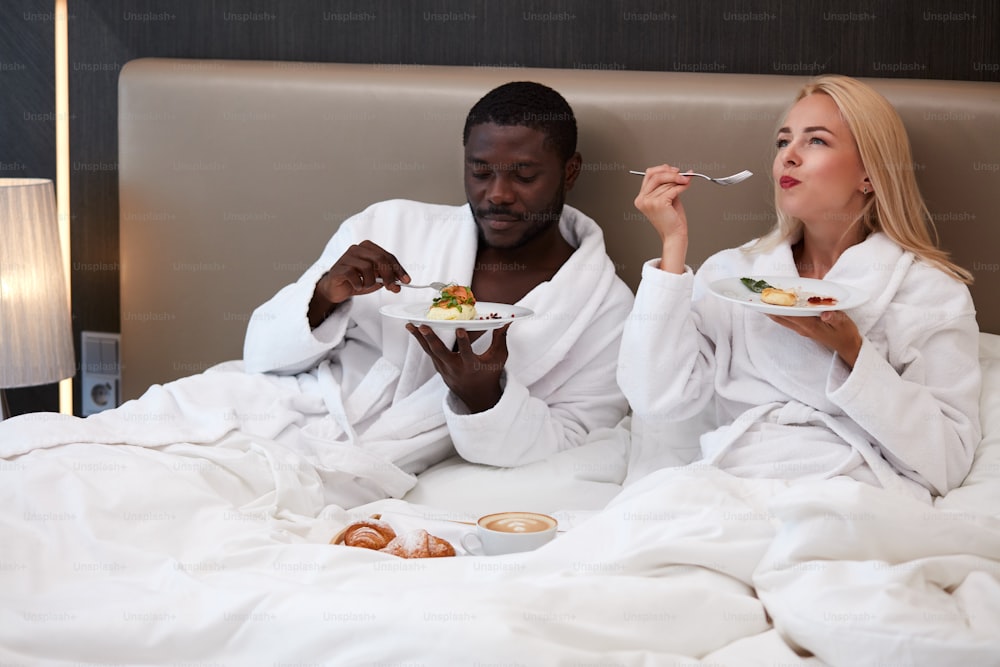 cute couple have breakfast together on bed, adorable caucasian lady happy with african husband, they are in love