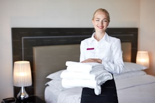 maid restores order and cleanliness in the hotel room, blonde caucasian woman looks at camera and smile. indoors