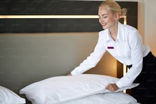 beautiful housemaid changes the pillowcase on the bed, caucasian blonde female in uniform prepares room for guests