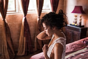 Woman with long black hair in white silk lingerie sitting on the bed in luxury hotel in the morning