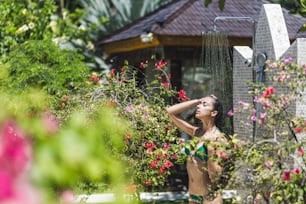 Donna che fa la doccia fuori nel verde tropicale giardino di Bali con molti fiori. Spruzzi di acqua pulita. Spa di lusso