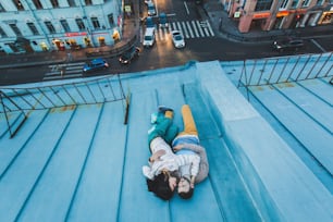 Young hipster couple lying on the roof and kissing. Beautiful view of the city from above. Casual style