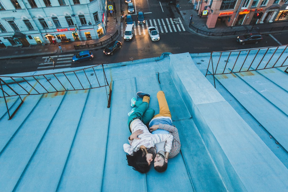 젊은 힙스터 커플이 지붕에 누워 키스를 하고 있다. 위에서 도시의 아름다운 전망. 캐주얼 스타일