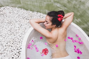 Woman relaxing in round outdoor bath with tropical flowers, organic skin care, luxury spa hotel, lifestyle photo