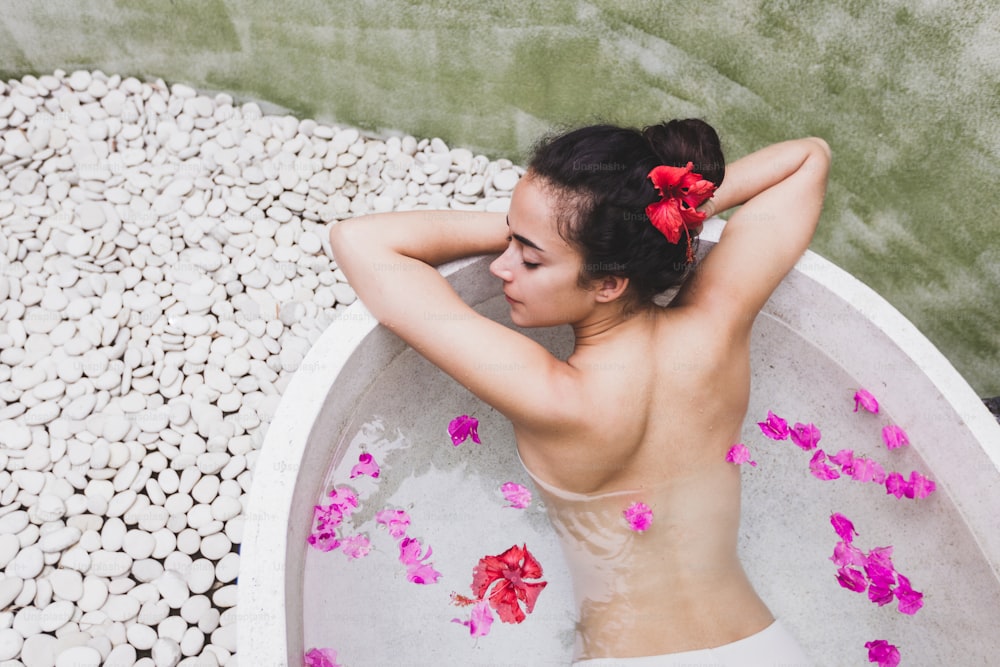 Woman relaxing in round outdoor bath with tropical flowers, organic skin care, luxury spa hotel, lifestyle photo