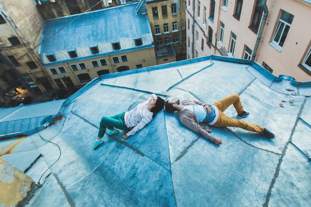 젊은 힙스터 커플이 지붕에 누워 키스를 하고 있다. 위에서 도시의 아름다운 전망. 캐주얼 스타일