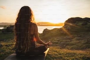 日の出の山で一人でヨガを瞑想する女性。後ろからの眺め。旅行ライフスタイルの精神的なリラクゼーションのコンセプト。自然との調和。