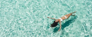 Mujer en bikini blanco acostada sobre la superficie del agua turquesa transparente en la playa. Concepto de viajes y vacaciones. Fondo tropical con espacio vacío