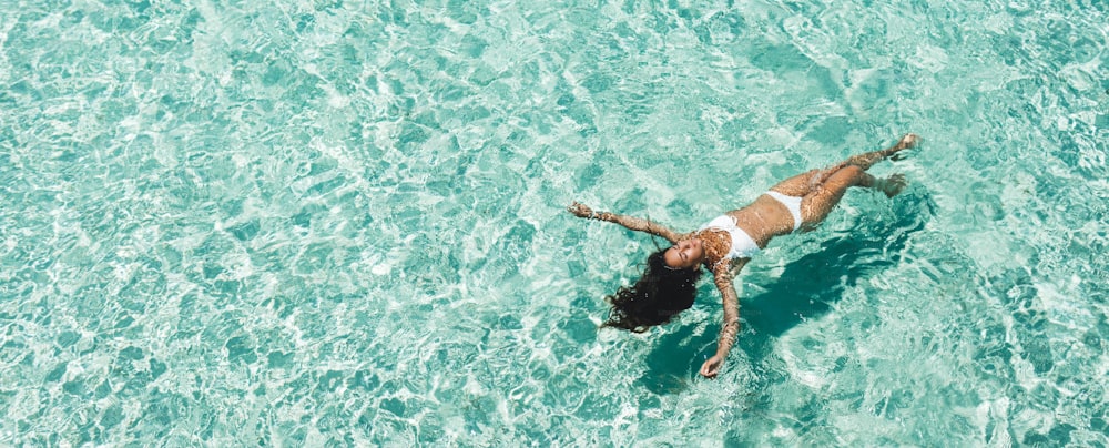 하얀 비키니를 입은 여자가 해변의 투명한 청록색 수면에 누워 있다. 여행과 휴가 개념. 빈 공간이 있는 열대 배경