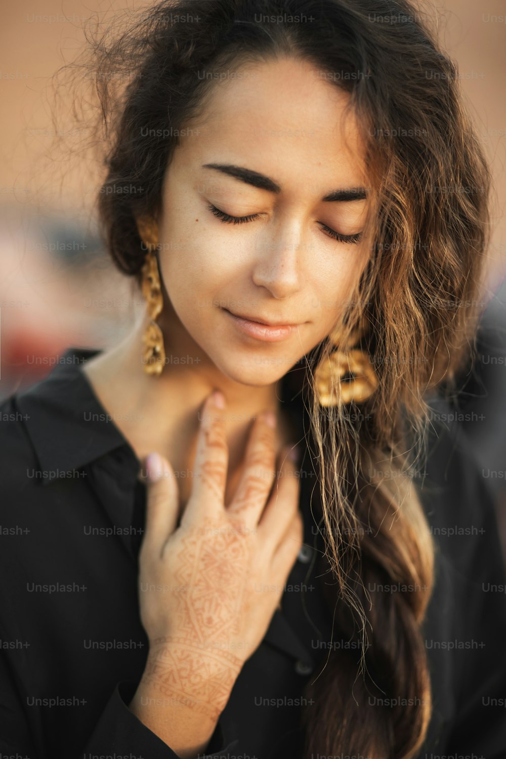 Close up portrait of young Asian brunette woman with long curly hair and closed eyes. Black shirt and golden earrings. Pretty female face and henna tattoo on hand.