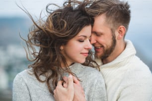 Close-up portrait of couple with wind in hair, hugging and happy together. Both in sweaters