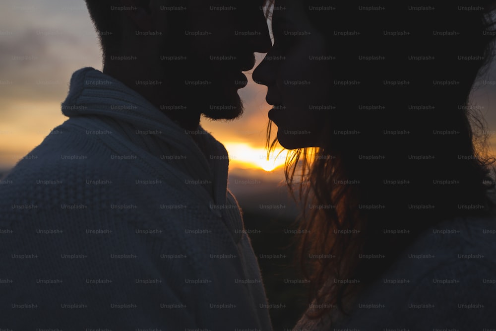 Gentle close-up portrait of man and woman together, happy, looking at each other. Silhouette at beautiful sunset light, wind in hair