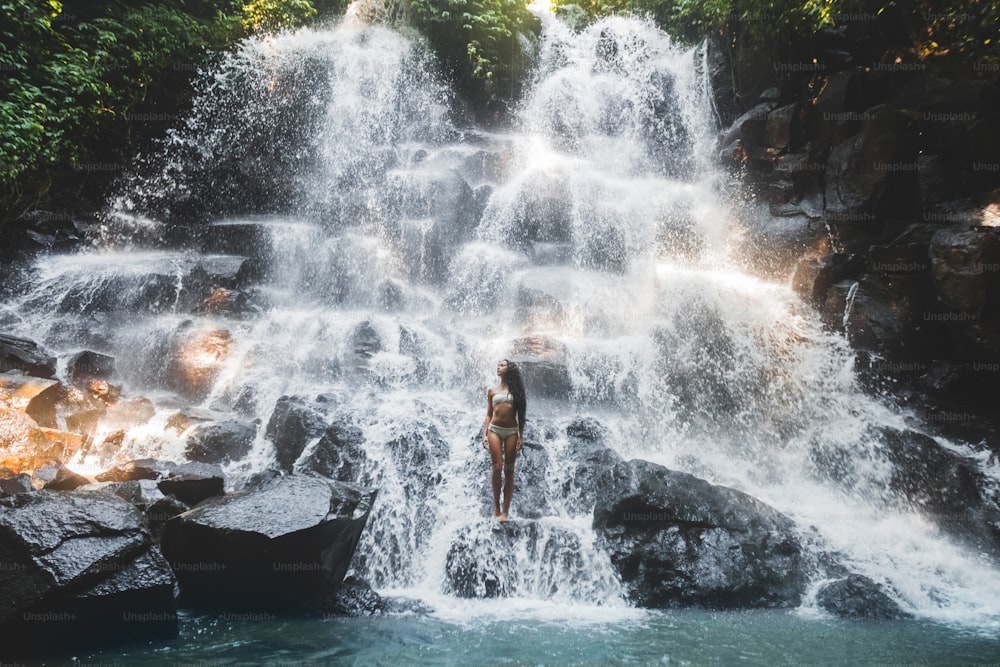 Mujer disfrutando bajo la corriente de una gran y hermosa cascada de cascada. Chica con cuerpo delgado y cabello largo. Kanto Lampo en el área de Ubud