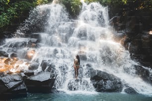 Frau genießt unter dem Strom des großen und schönen Wasserfalls. Mädchen mit schlankem Körper und langen Haaren. Kanto Lampo in der Gegend von Ubud