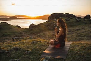 Frau, die alleine Yoga bei Sonnenaufgang mit Berg- und Meerblick macht. Harmonie mit der Natur. Selbstanalyse und Gewissenserforschung