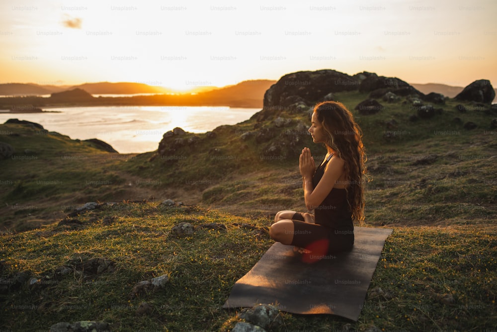 Donna che fa yoga da sola all'alba con vista sulle montagne e sull'oceano. Armonia con la natura. Autoanalisi e esame di coscienza