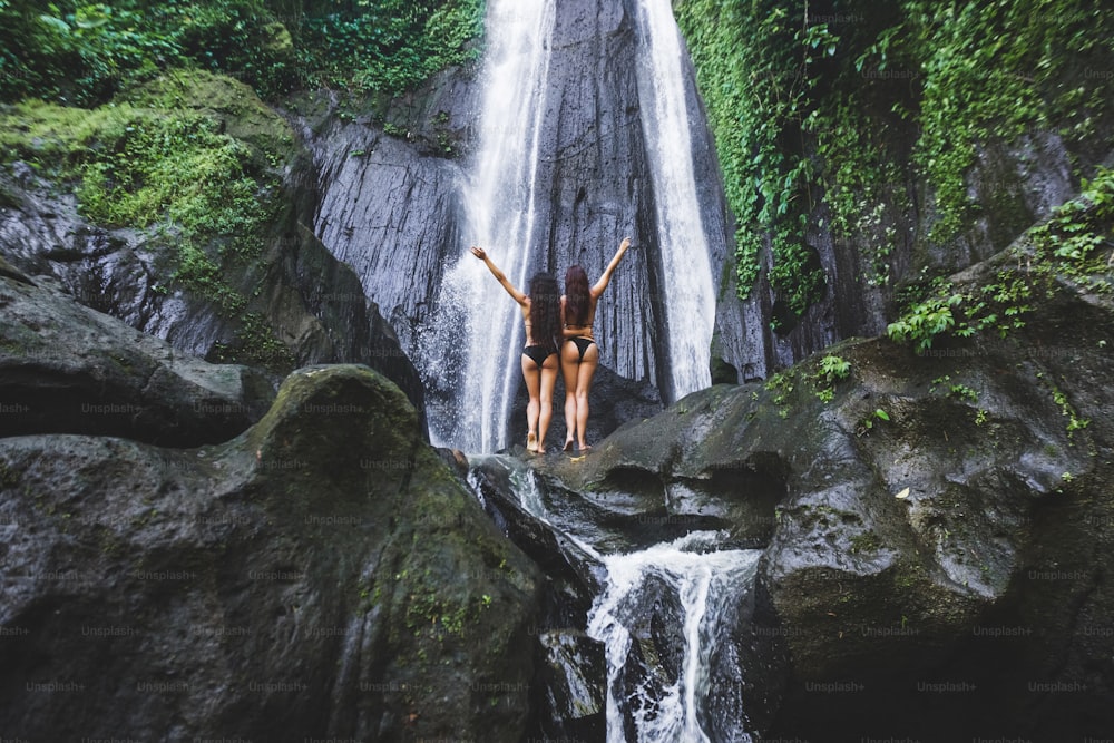 Due donne magre che si rilassano vicino alla bellissima cascata nella giungla di Bali. Avventura naturalistica Dusun Kuning nella zona di Ubud