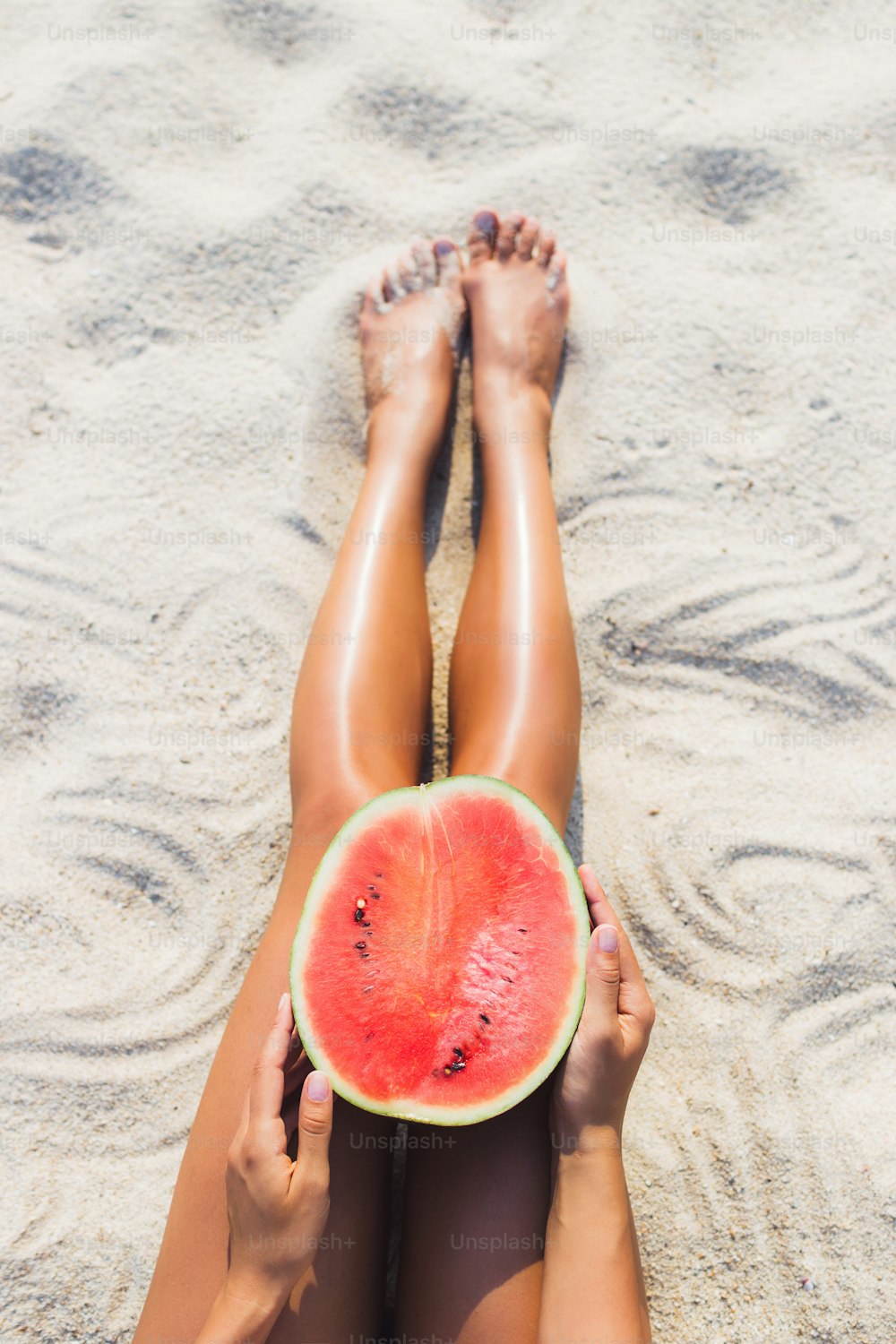 Frau mit halber Wassermelone am Strand