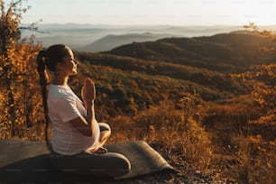 Spiritual and emotional concept of harmony with nature in maternity time. Pregnant woman praying alone outdoors on hill at sunset. Amazing autumn mountain view.