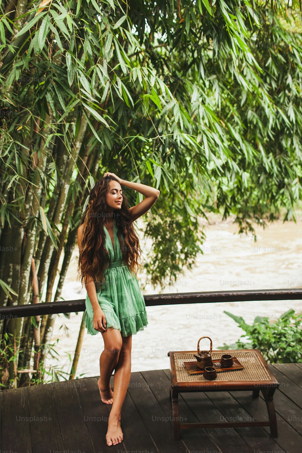 Schöne junge lockige authentische Frau im grünen Kleid trinkt gesunden Tee im Freien mit Naturhintergrund. Relax-Zeit-Konzept.