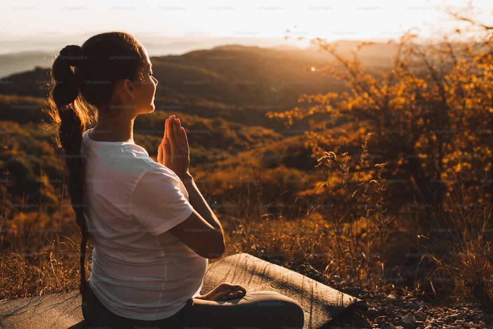 Spiritual and emotional concept of harmony with nature in maternity time. Pregnant woman praying alone outdoors on hill at sunset. Amazing autumn mountain view.