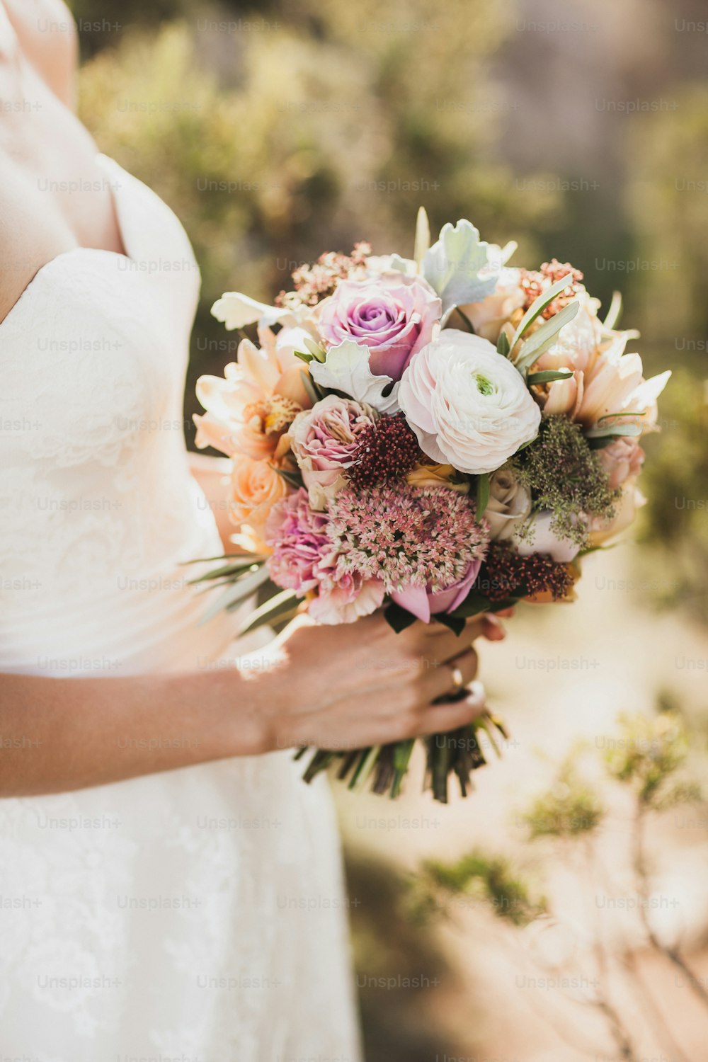 Sposa che tiene in mano piccolo bouquet da sposa nei colori arancioni autunnali. Rose rosa e arancioni, peonia bianca, fiori secchi e foglie.